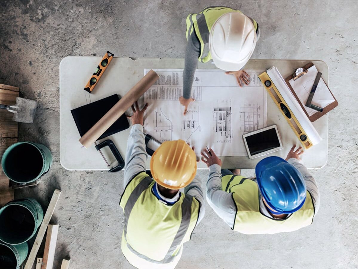 Top-down view of construction workers around a table with blueprints